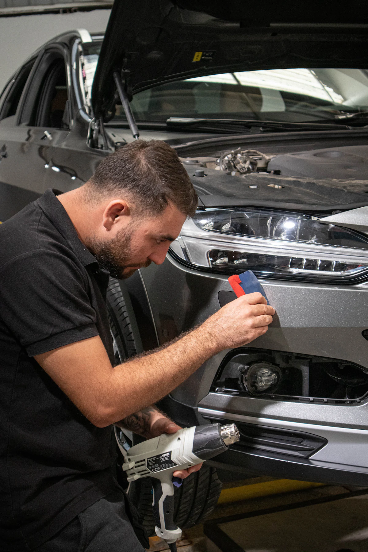 Installer squeegeeing clear film onto a grey front bumper
